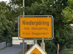 Gelbes Ortsschild mit der Aufschrift „Niederpöring, Gde. Oberpöring, Kreis Deggendorf“ vor grünem Hintergrund.