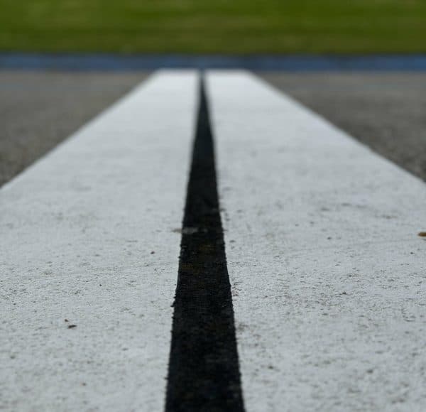 Zwei weiße Straßenmarkierungen auf Asphalt, Nahaufnahme mit unscharfem grünem Hintergrund.
