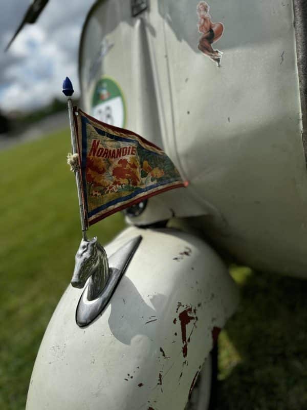 Kleine Fahne an einem alten weißen Motorroller, befestigt an einem verzierten Emblem, im Freien auf grünem Gras.