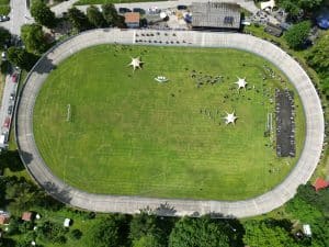 Luftaufnahme eines grünen Stadions mit Laufbahn, Sterndekorationen auf dem Rasen und einigen verstreuten Personen.