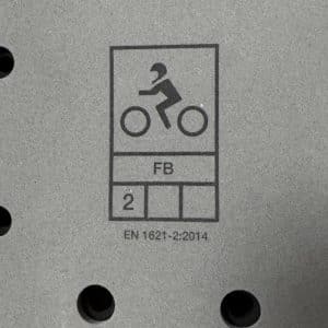Symbol eines Radfahrers mit der Beschriftung „FB“, der Zahl „2“ und dem Code „PN-1807-2.2014“ auf einer grauen, gelochten Oberfläche.