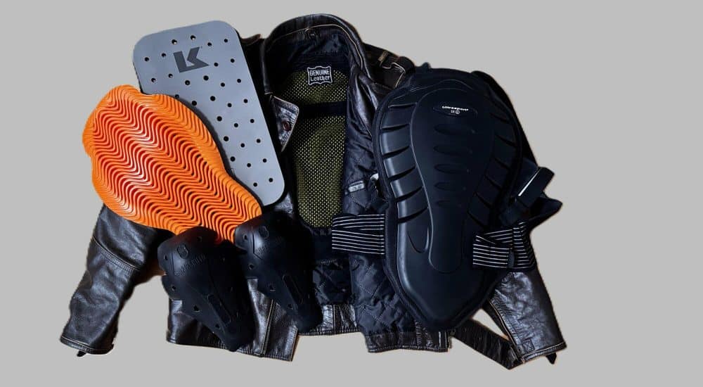 Motorradschutzkleidung mit verschiedenen Protektoren, darunter Rücken-, Schulter- und Ellenbogenschützer, auf grauem Hintergrund.