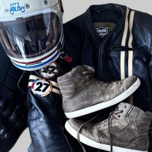 Motorradhelm, schwarze Lederjacke mit Streifen und graue Sneakers liegen aufeinander arrangiert.
