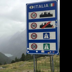 Schild mit Angaben von Tempolimit Italien mit Blick in ein Tal und See