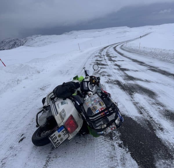 Lange kurvige schneebedeckte Straße durch weiße Felder mit seitlich liegender bepackter weißer Vespa