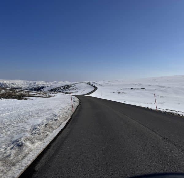 Lange, kurvenreiche Straße zum Nordkapp durch verschneite Felder unter klarem blauen Himmel – ein winterlicher Ausblick voller Ruhe und Weite