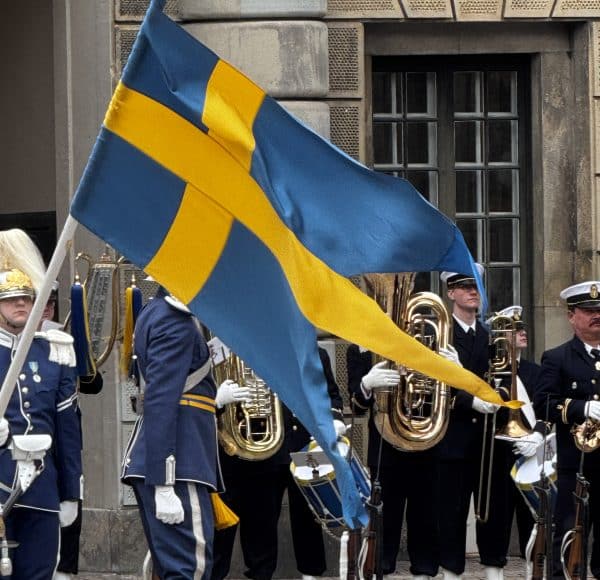 Eine schwedische Flagge wird bei einer Parade von Musikern in Uniformen im Freien getragen.