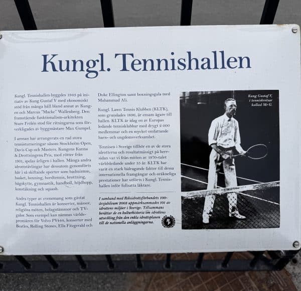 Informationstafel über die Kungliga Tennishallen mit Text und einem historischen Schwarzweißfoto eines Tennisspielers mit Schläger am Netz.