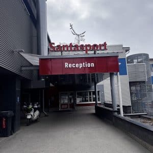Eingang zum Santapark mit rotem Schild „Reception“ und Rentierfigur oben auf dem Dach.