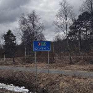 Straßenschild zeigt Richtung Rovaniemi, 33 km entfernt, vor bewölktem Himmel und kahlen Bäumen.