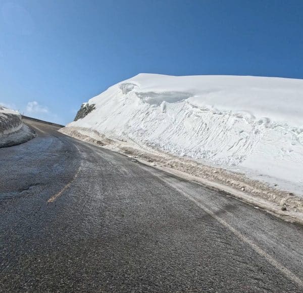 Verschneite Straße mit einer hohen Schneewehe am Straßenrand unter blauem Himmel.