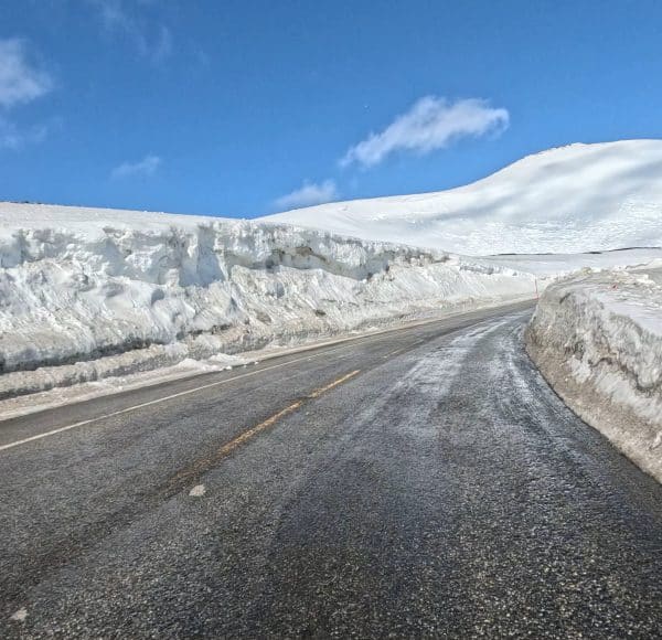 Verschneite Straße mit vereisten Spuren, hohe Schneewände an den Seiten, blauer Himmel mit wenigen Wolken.