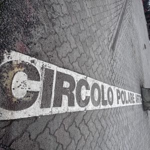 Weiße Markierung „CIRCOLO POLARE“ auf nassem Kopfsteinpflaster, fotografiert aus schrägem Winkel.
