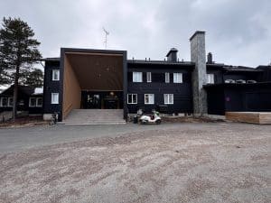Schwarzes, modernes zweistöckiges Gebäude mit überdachtem Eingang, Betonrampe und geparktem weißen Golfcart auf grauem Vorplatz unter bewölktem Himmel.
