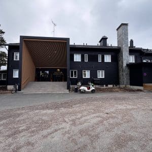 Schwarzes, modernes zweistöckiges Gebäude mit überdachtem Eingang, Betonrampe und geparktem weißen Golfcart auf grauem Vorplatz unter bewölktem Himmel.