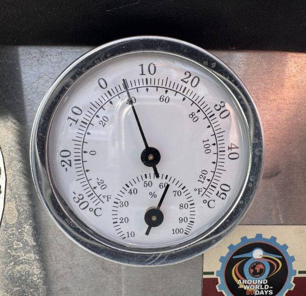 Rundes Thermometer zeigt etwa 15°C und 35% Luftfeuchtigkeit an, metallische Umrahmung, kleines Logo unten rechts.