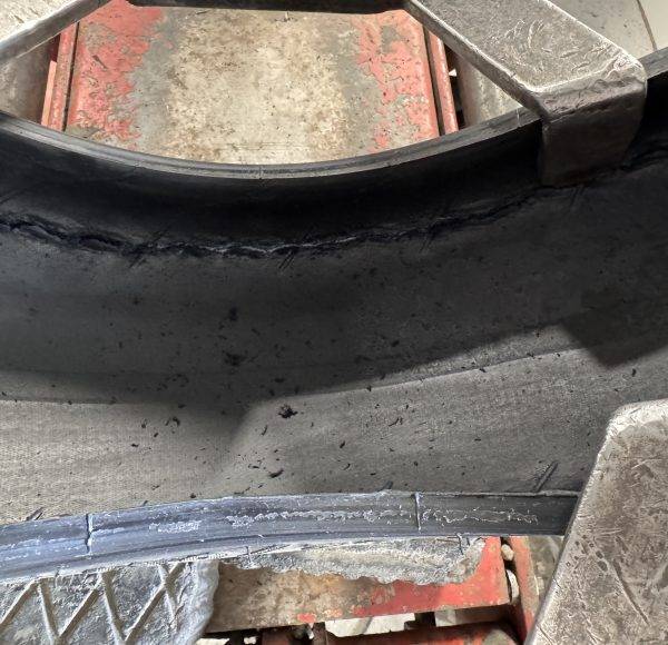 Nahaufnahme eines Autoreifens mit sichtbarem Riss und Verschleiß, aufgenommen in einer Werkstattumgebung.