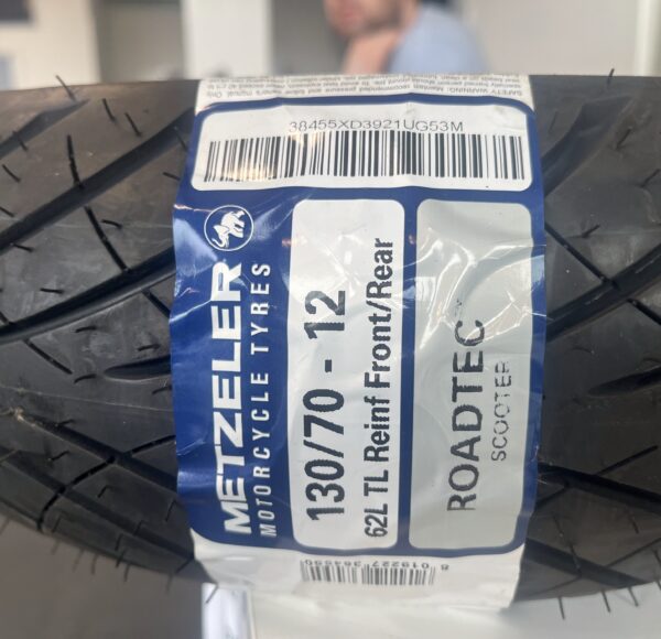Motorradreifen mit Etikett „Metzeler ROADTEC 130/70-12 TL Reinf Front/Rear“, Nahaufnahme, Fokus auf Reifengröße und Marke.