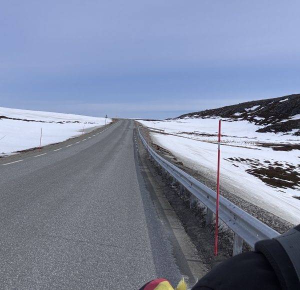 Leere Straße durch verschneite Landschaft unter bewölktem Himmel.