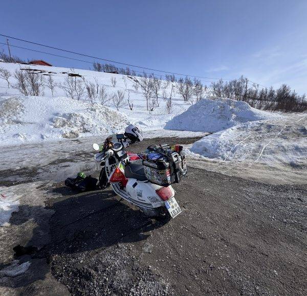 Motorrad mit Beiwagen steht auf schneebedecktem Parkplatz, umgeben von Schneehügeln und kahlen Bäumen unter klarem Himmel.