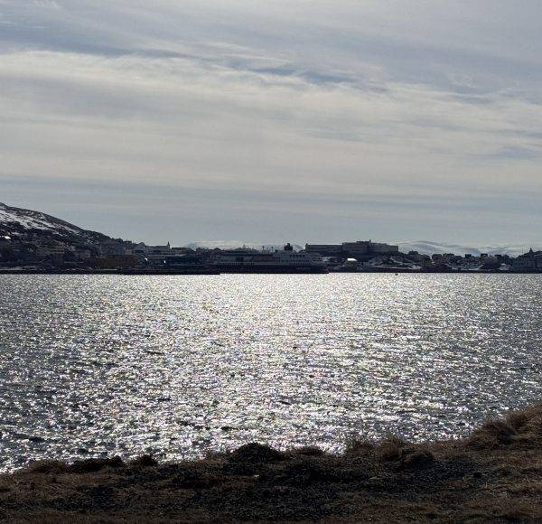 Sonnenschein spiegelt sich auf einem ruhigen See, Hügel im Hintergrund, teilweise bewölkter Himmel.