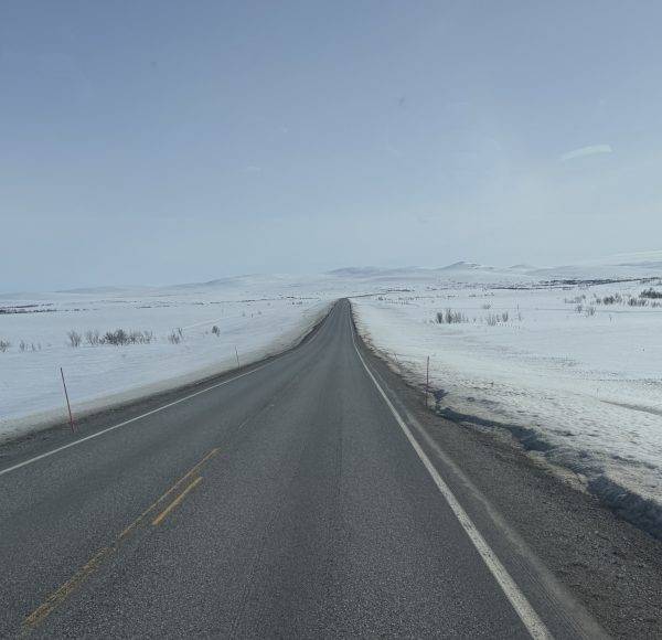 Eine gerade Straße führt durch eine schneebedeckte, flache Landschaft unter klarem Himmel.