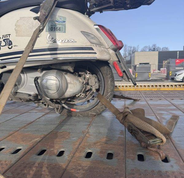 Ein beschädigter Motorroller ist mit Gurten auf einem Abschleppwagen befestigt, das Hinterrad fehlt.