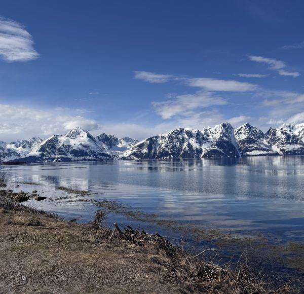 Verschneite Berge spiegeln sich in einem ruhigen See unter klarem, blauem Himmel.