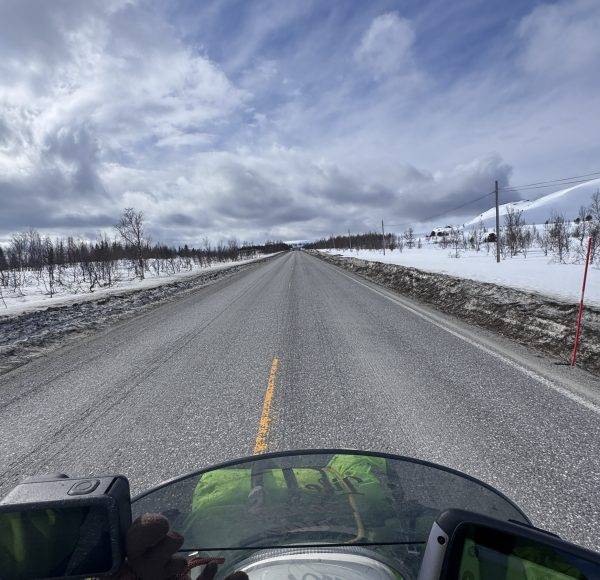 Gerade Straße im Winter, Schnee an den Seiten, bewölkter Himmel, Foto aus der Sicht eines Motorradfahrers.