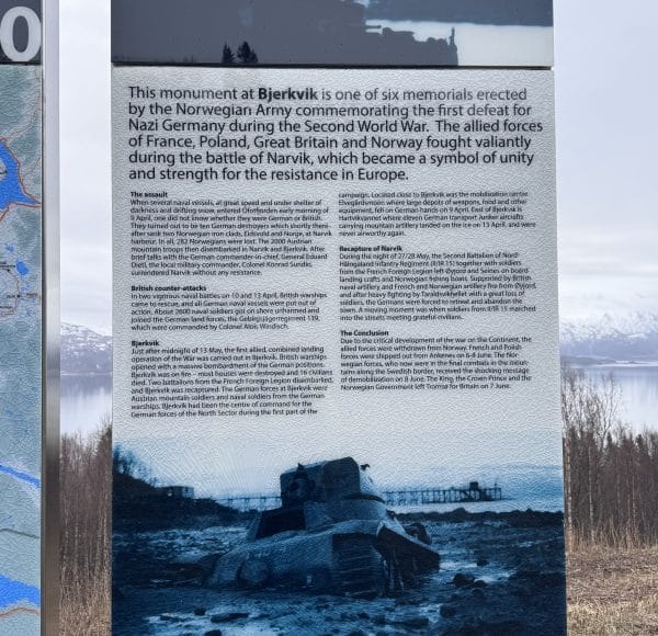 Informationstafel über das Schlachtschiff Tirpitz bei Narvik, mit englischem und norwegischem Text, historischem Foto und winterlicher Landschaft im Hintergrund.