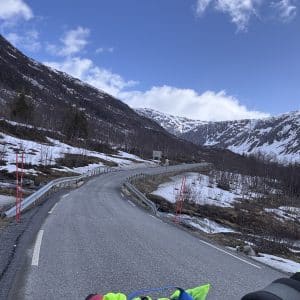 Kurvige Bergstraße mit Schnee an den Seiten, umgeben von Bergen unter blauem Himmel mit Wolken.