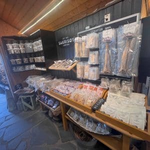 Ein Ladenregal mit verschiedenen verpackten Produkten, darunter Snacks und Süßigkeiten, ordentlich auf Holztischen und Regalen ausgestellt.