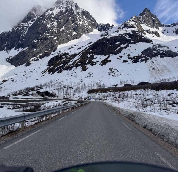 Eine Straße führt durch eine verschneite Berglandschaft mit schroffen Gipfeln und blauem Himmel im Hintergrund.