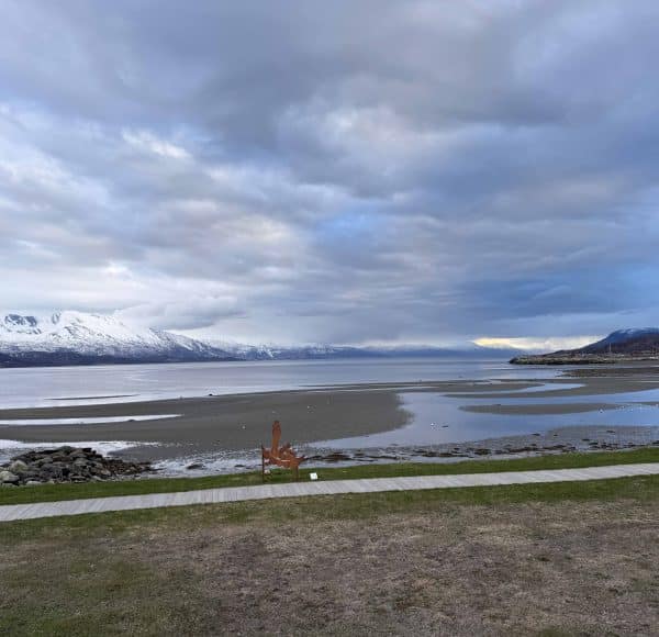 Weite Landschaft mit Bergen im Hintergrund, Wolken am Himmel und einem ruhigen See im Vordergrund.