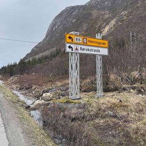 Straßenschild mit Ortsname „Bremanger“ neben einer Landstraße, im Hintergrund Berge und spärliche Vegetation.