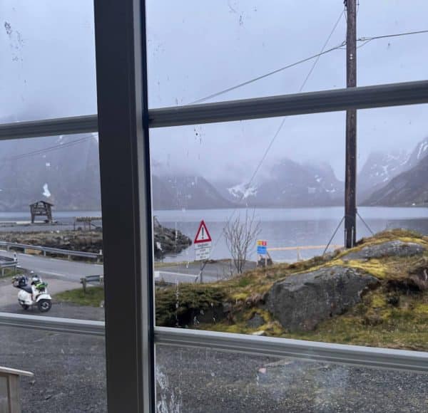 Blick durch ein Fenster auf eine neblige Landschaft mit Bergen, Wasser, Straßen und Verkehrsschildern.