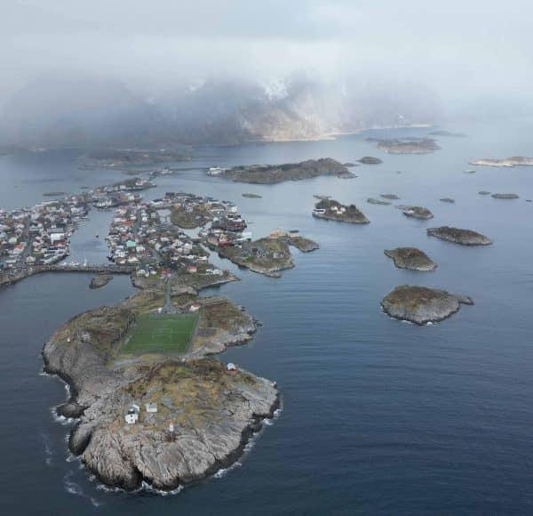 Luftaufnahme von kleinen Inseln mit Häusern im Meer, umgeben von Nebel und Bergen im Hintergrund.