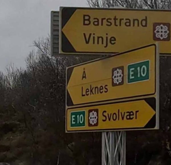 Gelbe Straßenschilder mit Richtungen nach Barstrand, Vinje, Å, Leknes und Svolvær sowie E10-Route in ländlicher Umgebung.