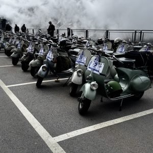 Viele klassische Motorroller sind in Parkbuchten nebeneinander aufgereiht, nummerierte Schilder an den Lenkern, mit leicht nebligem Hintergrund.