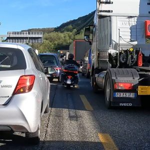Autos, LKW und ein Motorrad stehen auf einer mehrspurigen Straße im Stau, bei Tageslicht und gutem Wetter.