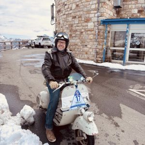 Olaf H. Just mit Lederjacke und Helm fährt seine Faro Basso im Schnee vor einem Steingebäude der Edelweissspitze.