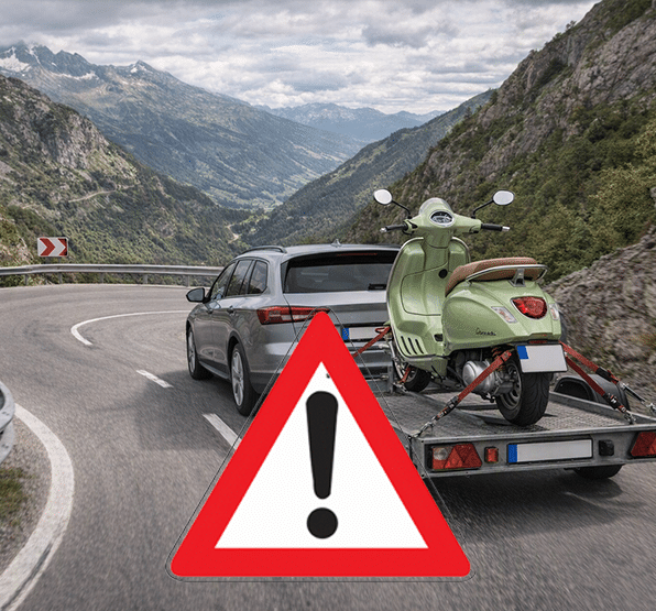 Auto mit Anhänger und Roller fährt auf kurviger Bergstraße, Warnschild mit Ausrufezeichen im Vordergrund.