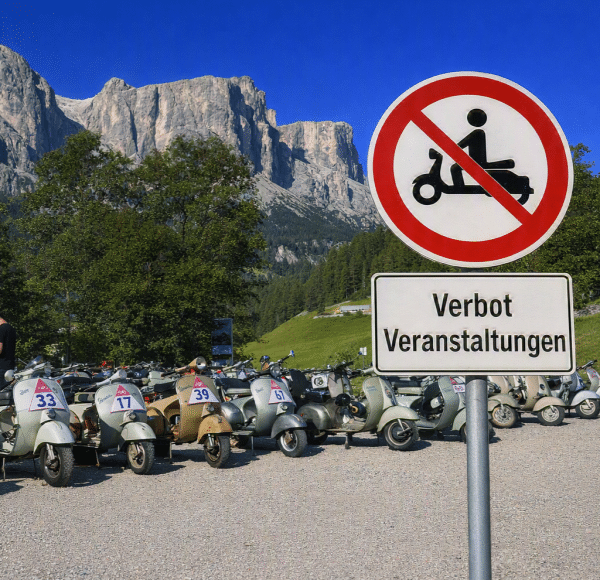 Mehrere Motorroller vor einem Verbotsschild mit Text „Verbot Veranstaltungen“ in einer bergigen Landschaft bei klarem Himmel.