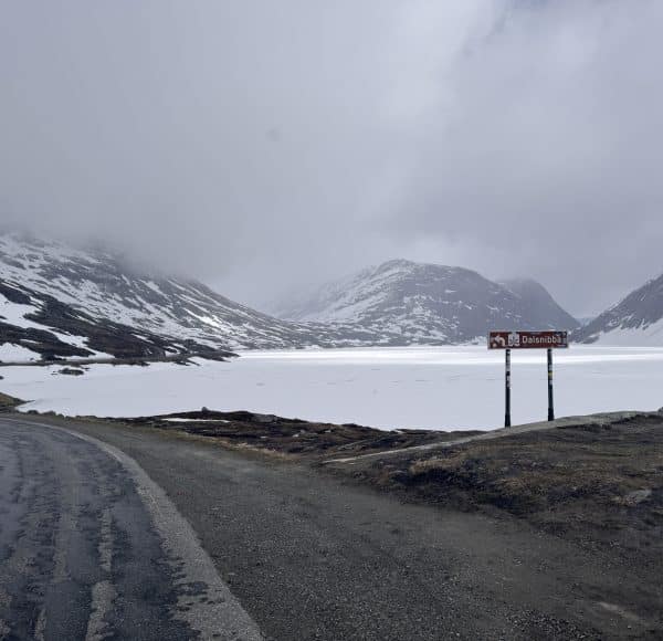 Verschneite Berge mit gefrorenem See, grauer Himmel und ein rotes Schild mit der Aufschrift „Dalsnibba“.