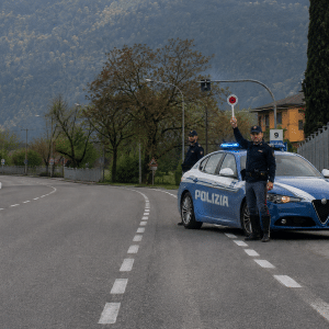 Zwei Polizisten stehen neben einem Streifenwagen mit Blaulicht auf einer Landstraße vor Bergen und Bäumen. © JustKommunikation GmbH | JustRide it