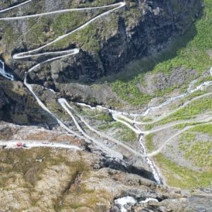 Trollstigen Serpentinen windet sich durch steile, felsige Berge mit Wasserfall und grünem Tal im Hintergrund, aus der Vogelperspektive aufgenommen. © JustKommunikation GmbH | JustRide it