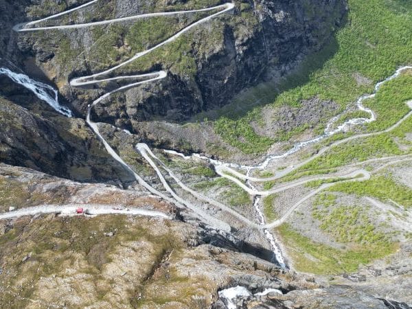 Trollstigen Serpentinen windet sich durch steile, felsige Berge mit Wasserfall und grünem Tal im Hintergrund, aus der Vogelperspektive aufgenommen. © JustKommunikation GmbH | JustRide it